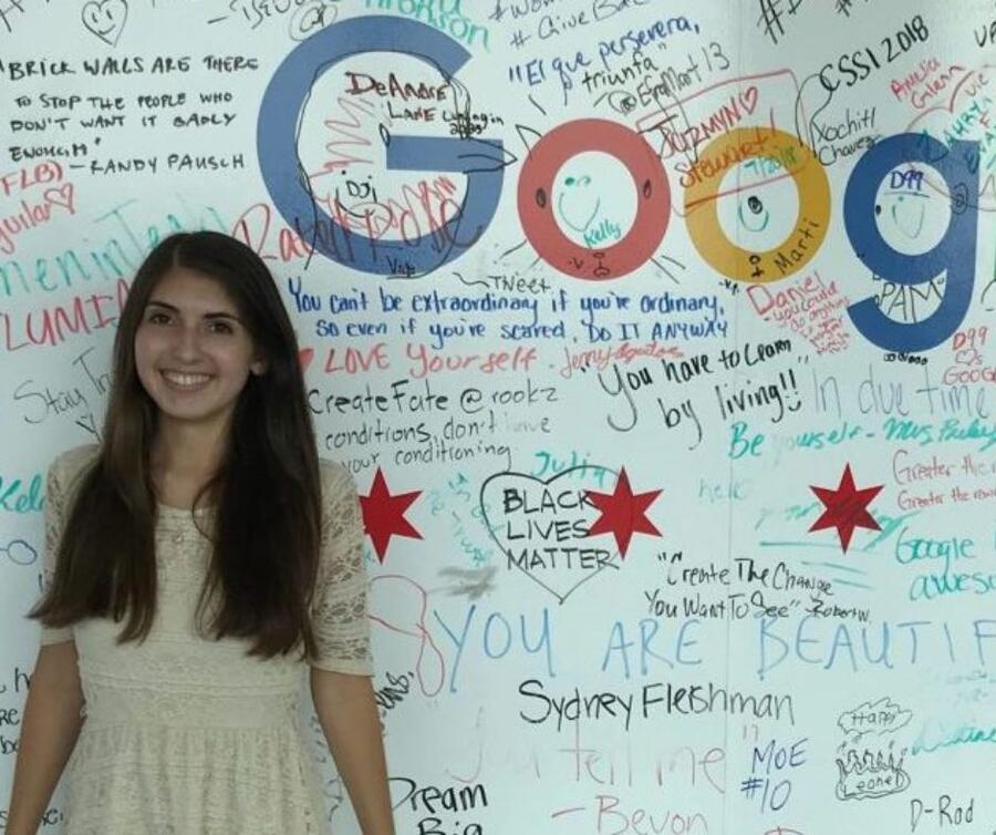 A grinning student positioned before a Google signboard, where individuals share their experiences.)