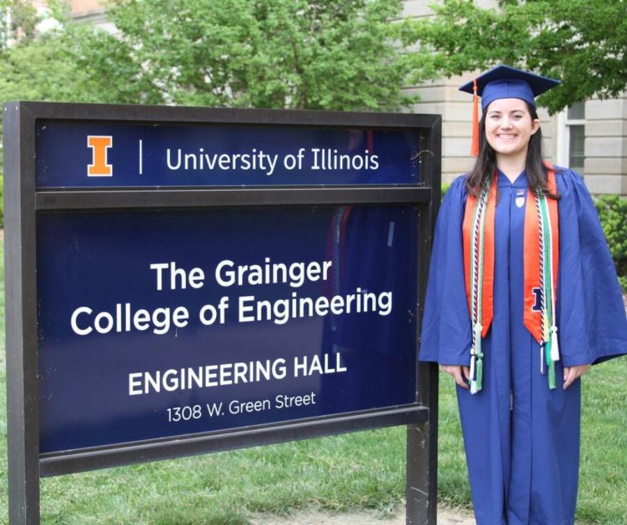 A student wearing a cap and gown stands next to a sign for the Grainger Engineering.
