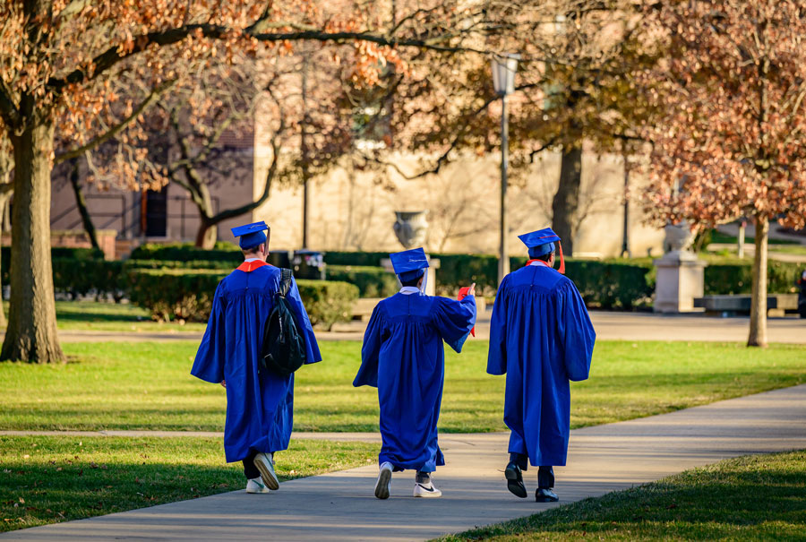 3 students in Illinois graduation gowns walking across the main quad on a sunny day